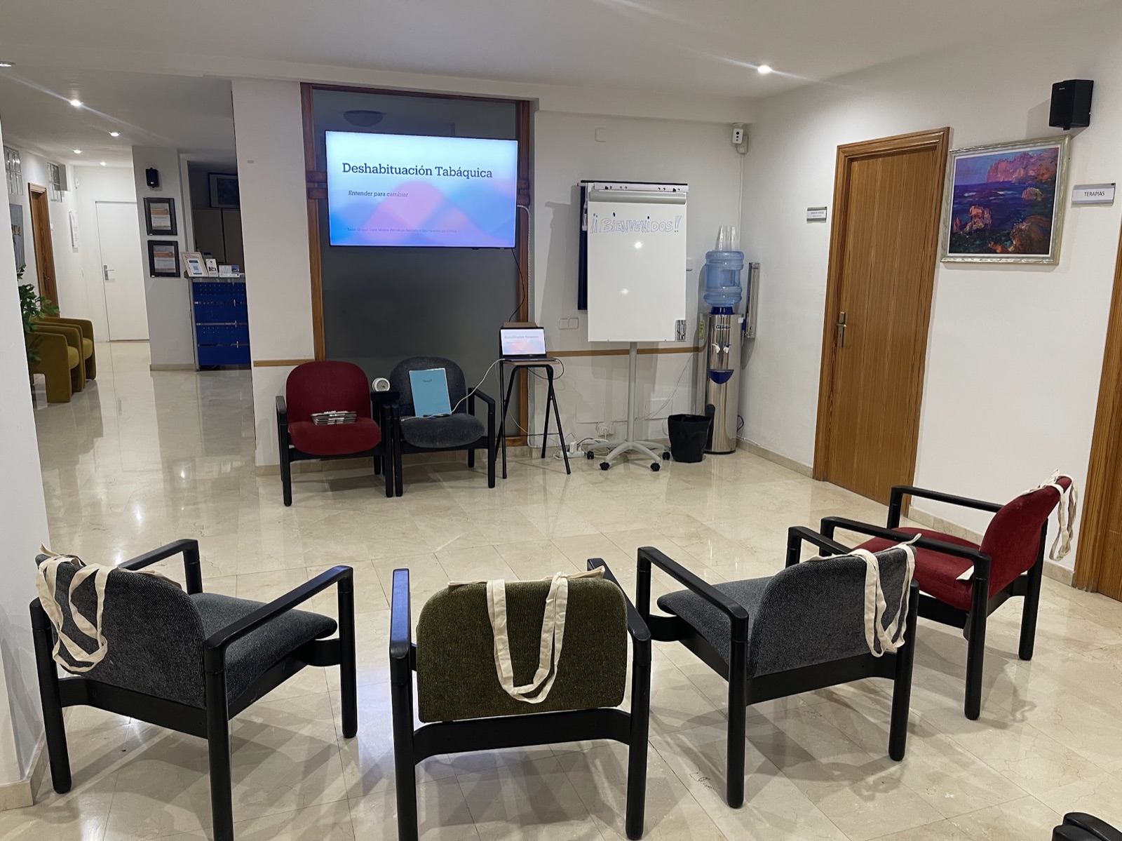 Sala preparada para un taller grupal de Irene Molina, con sillas en círculo y una pantalla con la presentación de deshabituación tabáquica
