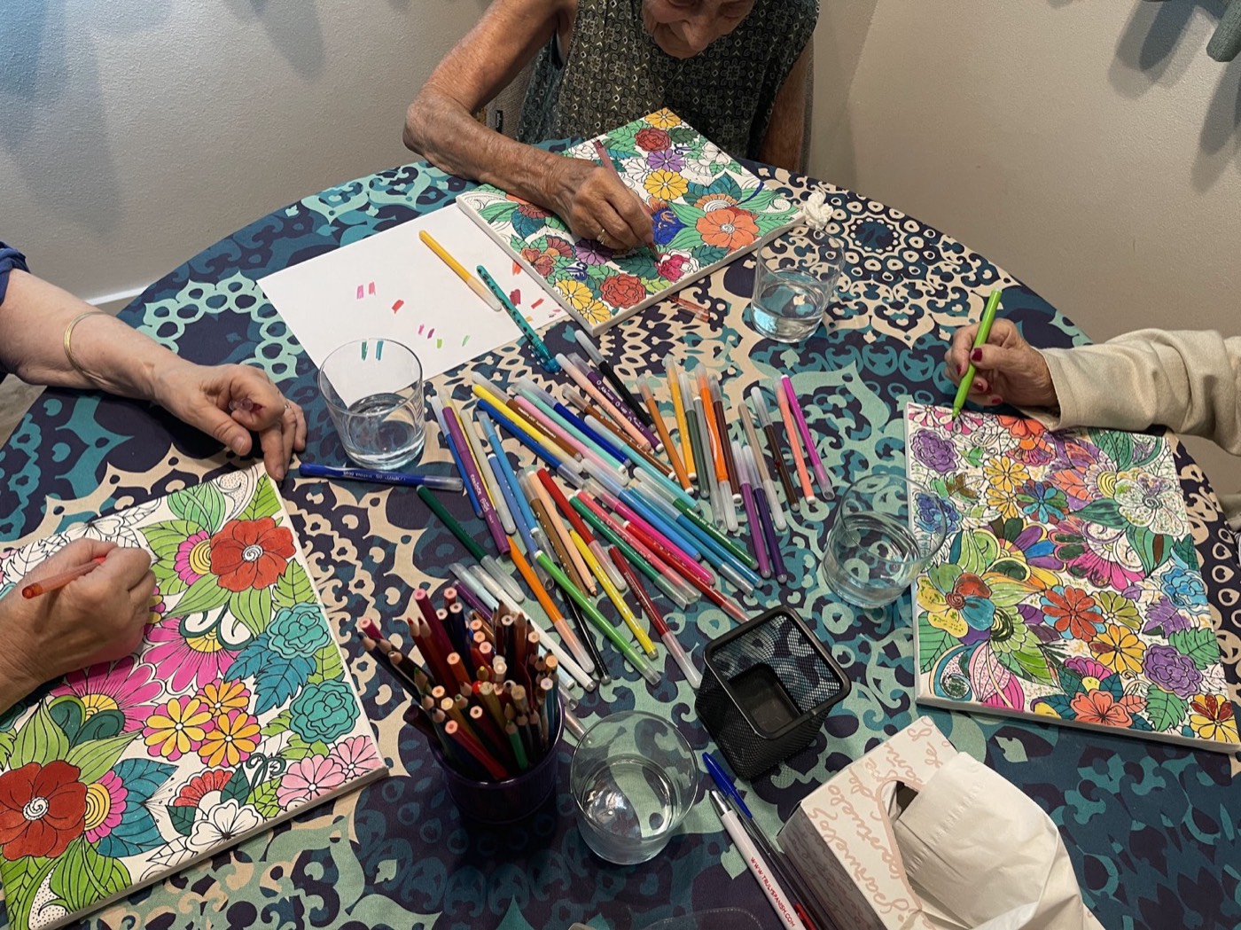 Manos de varias personas coloreando mandalas con lápices de colores alrededor de una mesa, durante una sesión de rehabilitación neuropsicológica