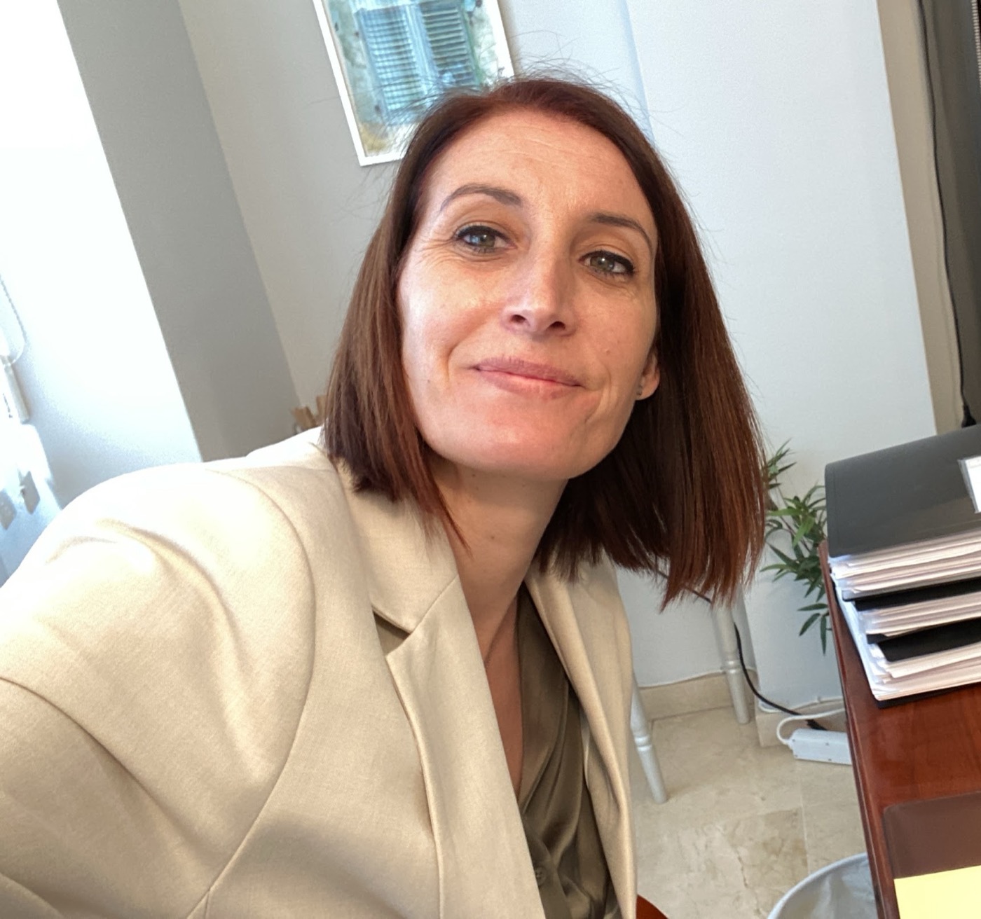 Psicóloga sonriendo en su despacho, junto a un escritorio con carpetas y estanterías