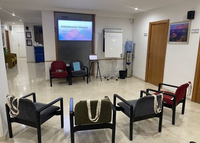 Sala preparada para un taller grupal de Irene Molina, con sillas en círculo y una pantalla con la presentación de deshabituación tabáquica