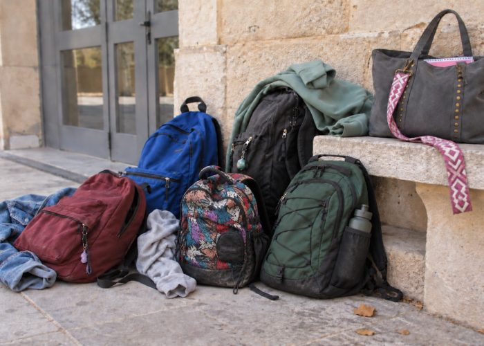 Mochilas, un bolso y prendas de adolescentes junto a un banco de piedra a la entrada de un instituto